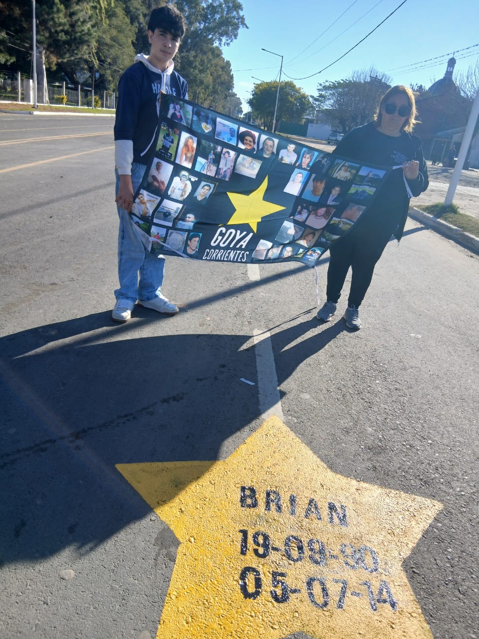 Detalle de una estrella amarilla con nombre y fechas junto a la bandera con las fotos de las víctimas